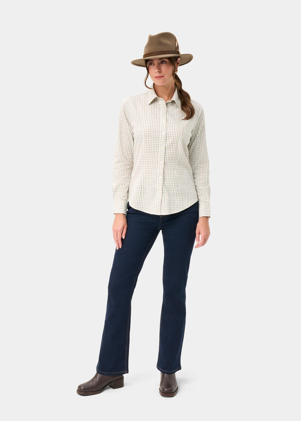 Woman in a brown hat, Bromford Olive Check Shirt, dark jeans, and boots stands against a plain white background.