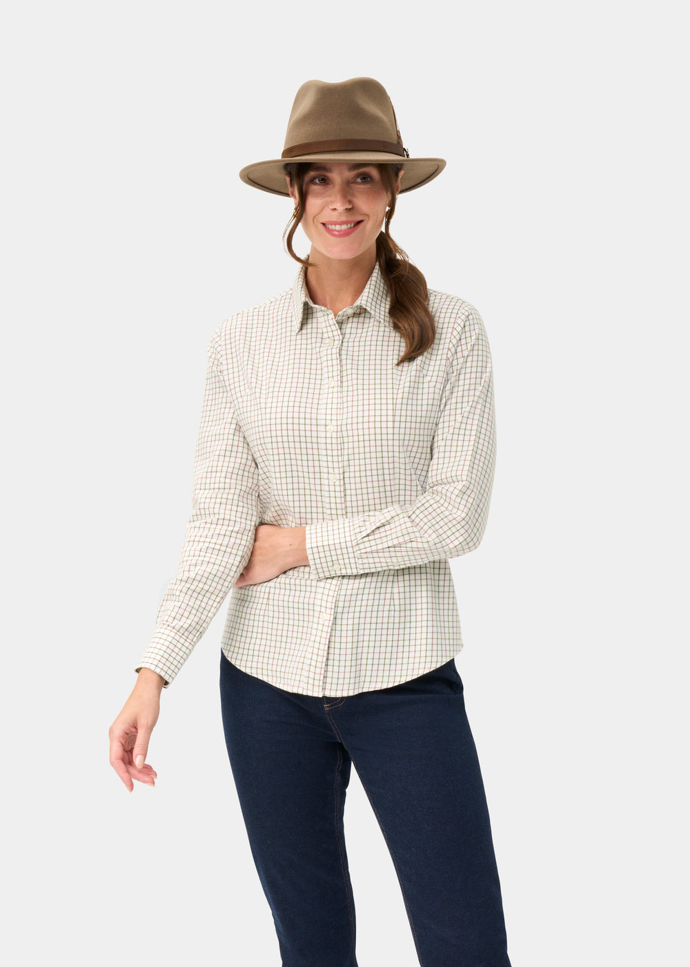 Woman in the Bromford Ladies Cotton Shirt in Olive Check, tan hat, and dark jeans smiles against a light background.