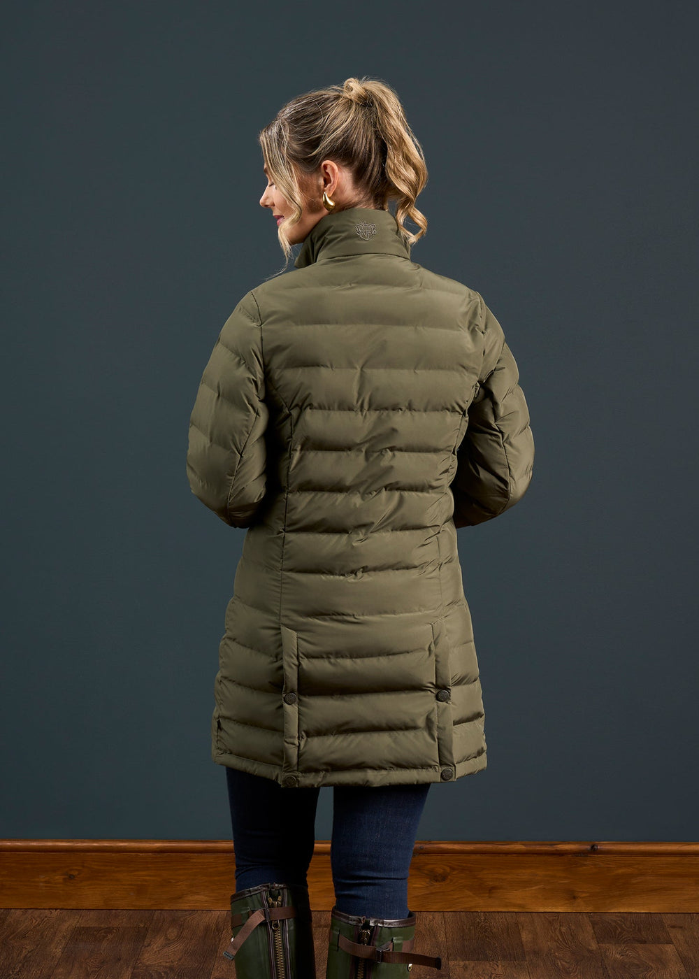 Woman with blonde ponytail wears Calsall Ladies Coat in Olive, Regular Fit, water repellent, facing away from camera.
