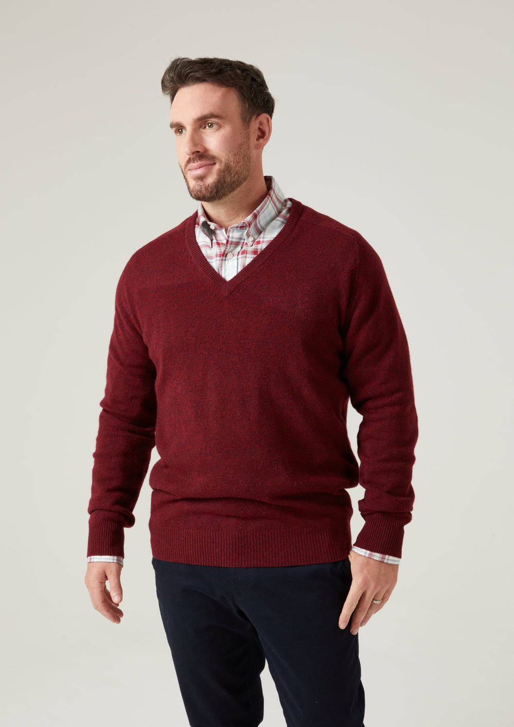 Man in a red Hampshire Lambswool Vee Neck Jumper, classic fit, stands against a plain light background, looking aside.