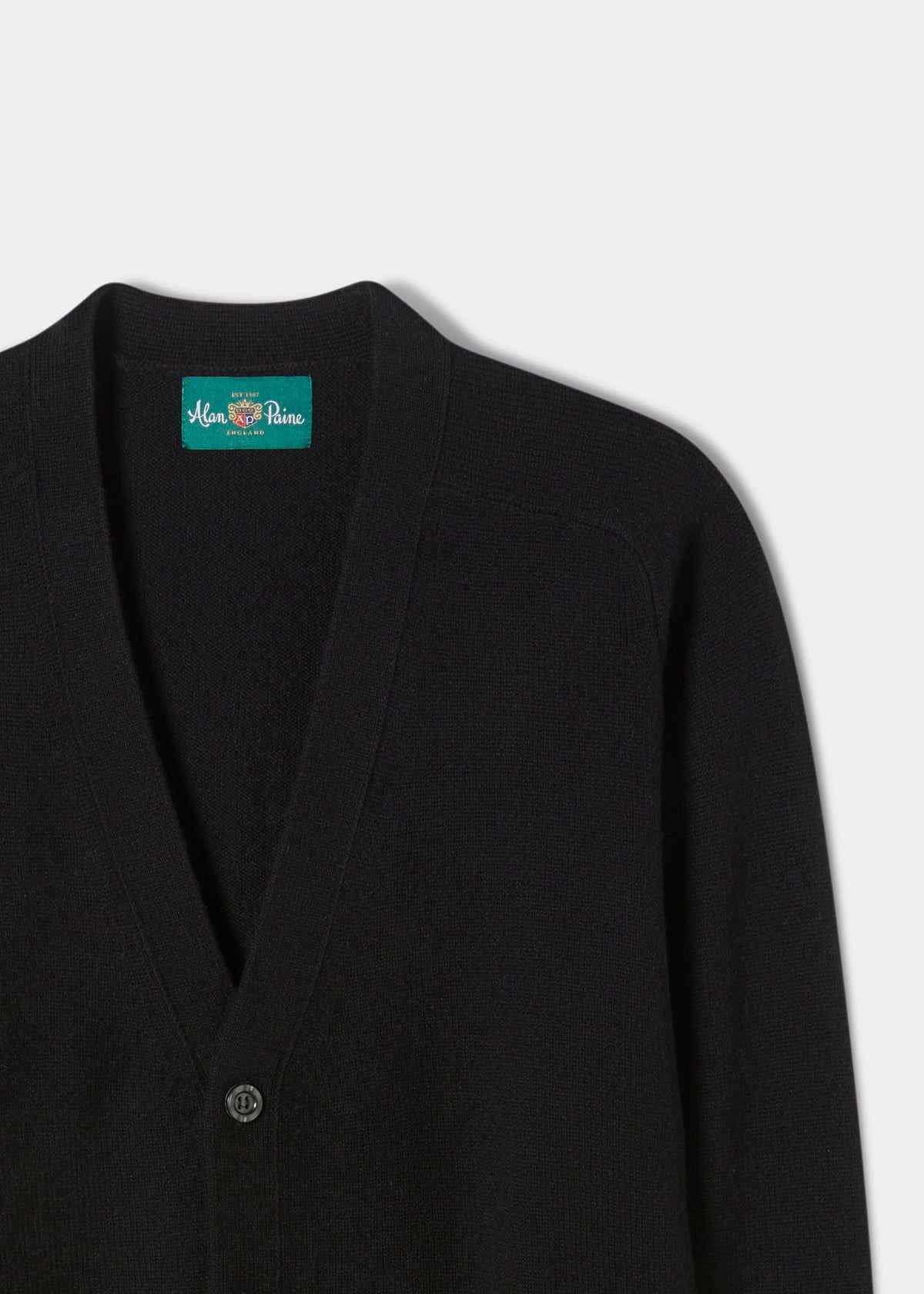 Cornwall Lambswool V-Neck Cardigan in black, classic fit, single button, green collar label, on white background.