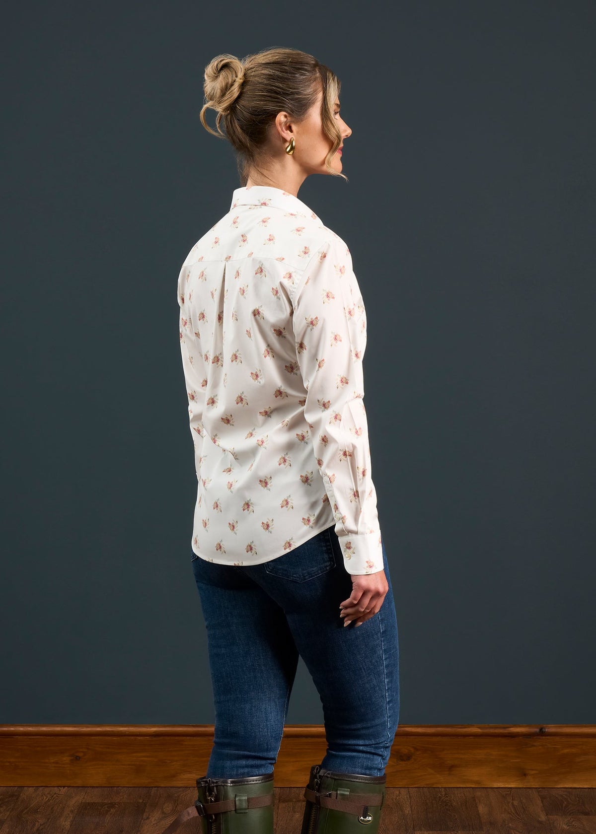 Woman in Lawen Cotton Printed Shirt in Floral Print, jeans, and boots stands sideways by a dark gray wall and wood floor.