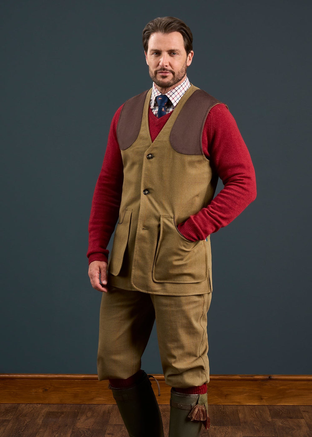 A man in a red sweater and Axford Men’s Waterproof Lightweight Shooting Waistcoat in Aspen stands against a dark backdrop.