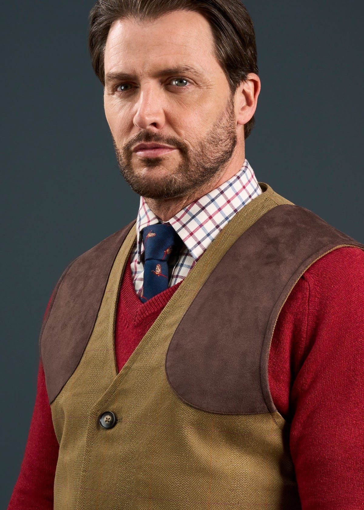 Man with brown hair in red sweater, plaid shirt, tie, and Axford Men’s Waterproof Lightweight Shooting Waistcoat in Aspen.