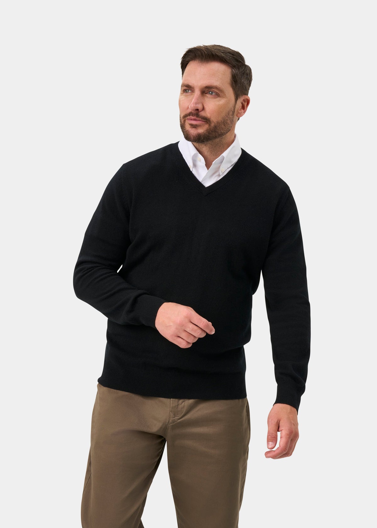 Man in Haddington Pure Cashmere V-Neck Jumper in black and khakis stands against light gray, looking to the side.