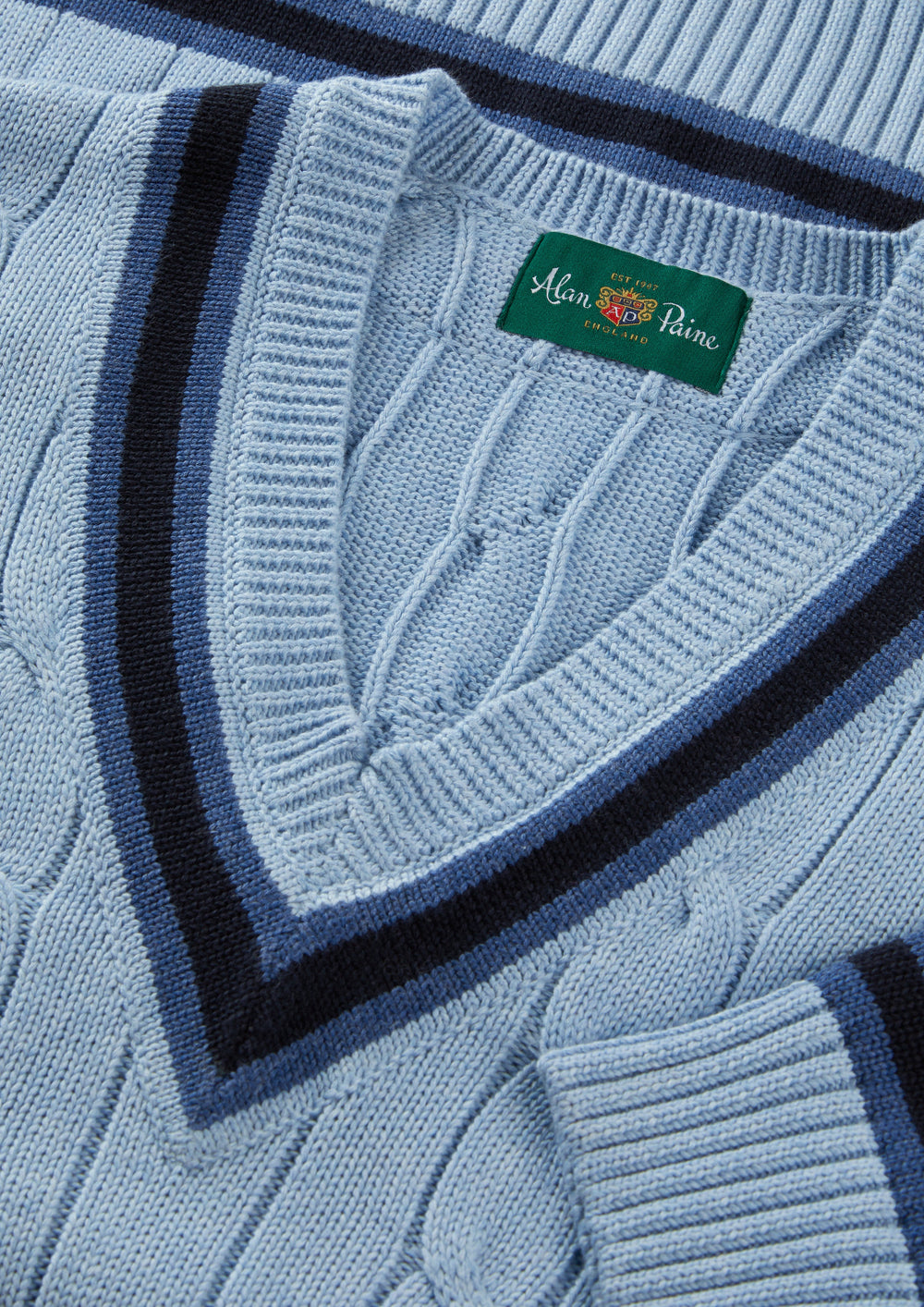 Steel blue cotton cable knit V-neck jumper by Alan Paine, featuring dark navy striped trim and ribbed neckline, close-up view