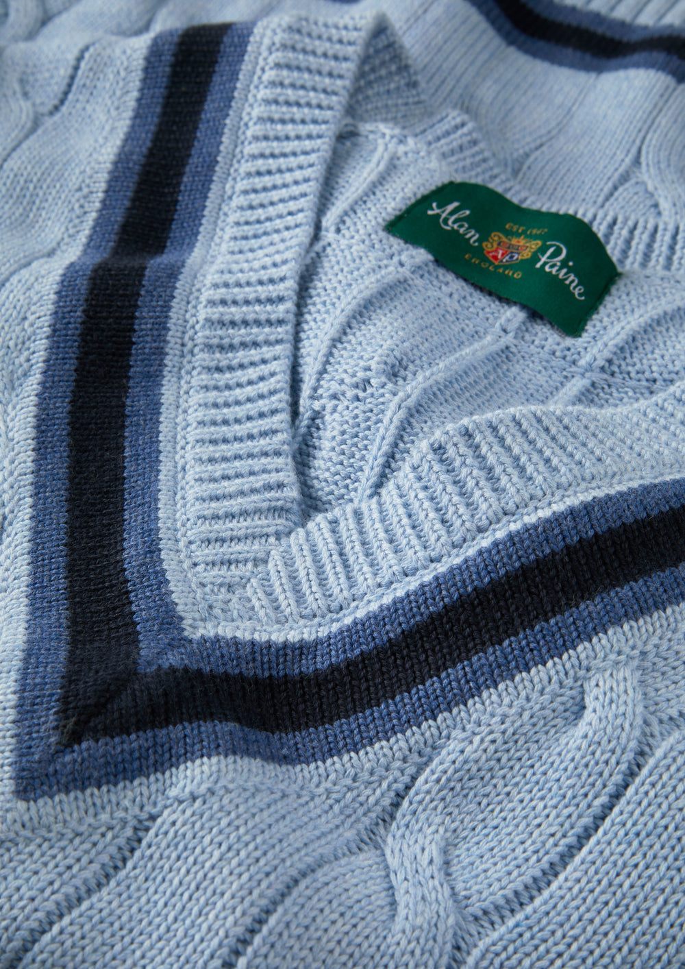Steel blue and dark navy cotton cable knit V-neck jumper by Alan Paine, featuring ribbed trim and striped detailing, close-up view
