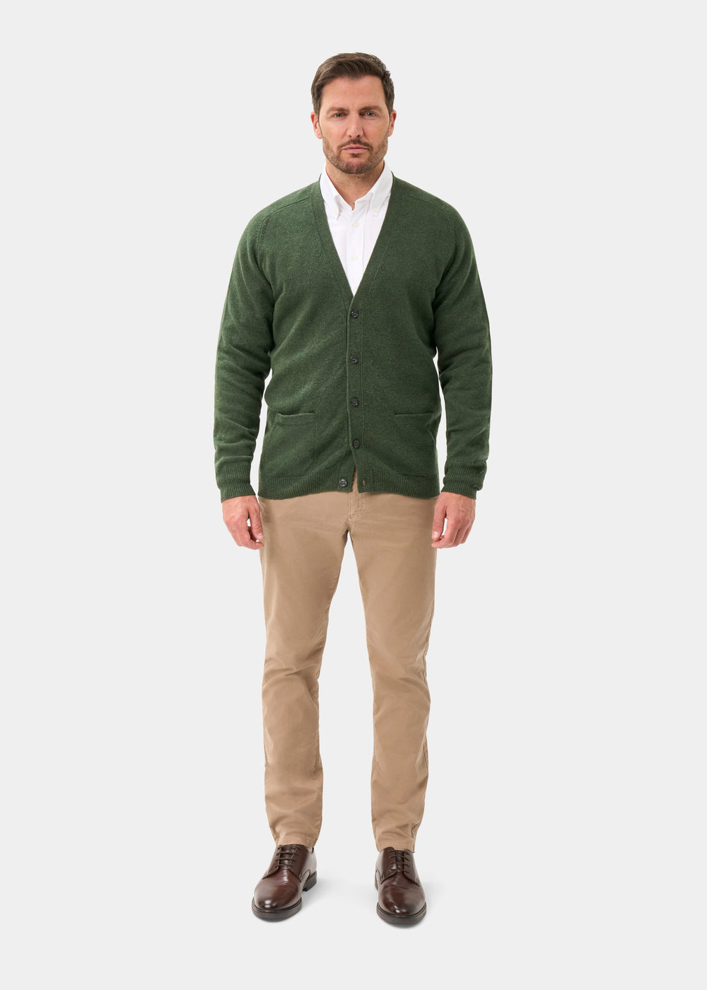 Man wearing Cornwall Lambswool V-Neck Cardigan in Rosemary, white shirt, khaki pants, and brown dress shoes.