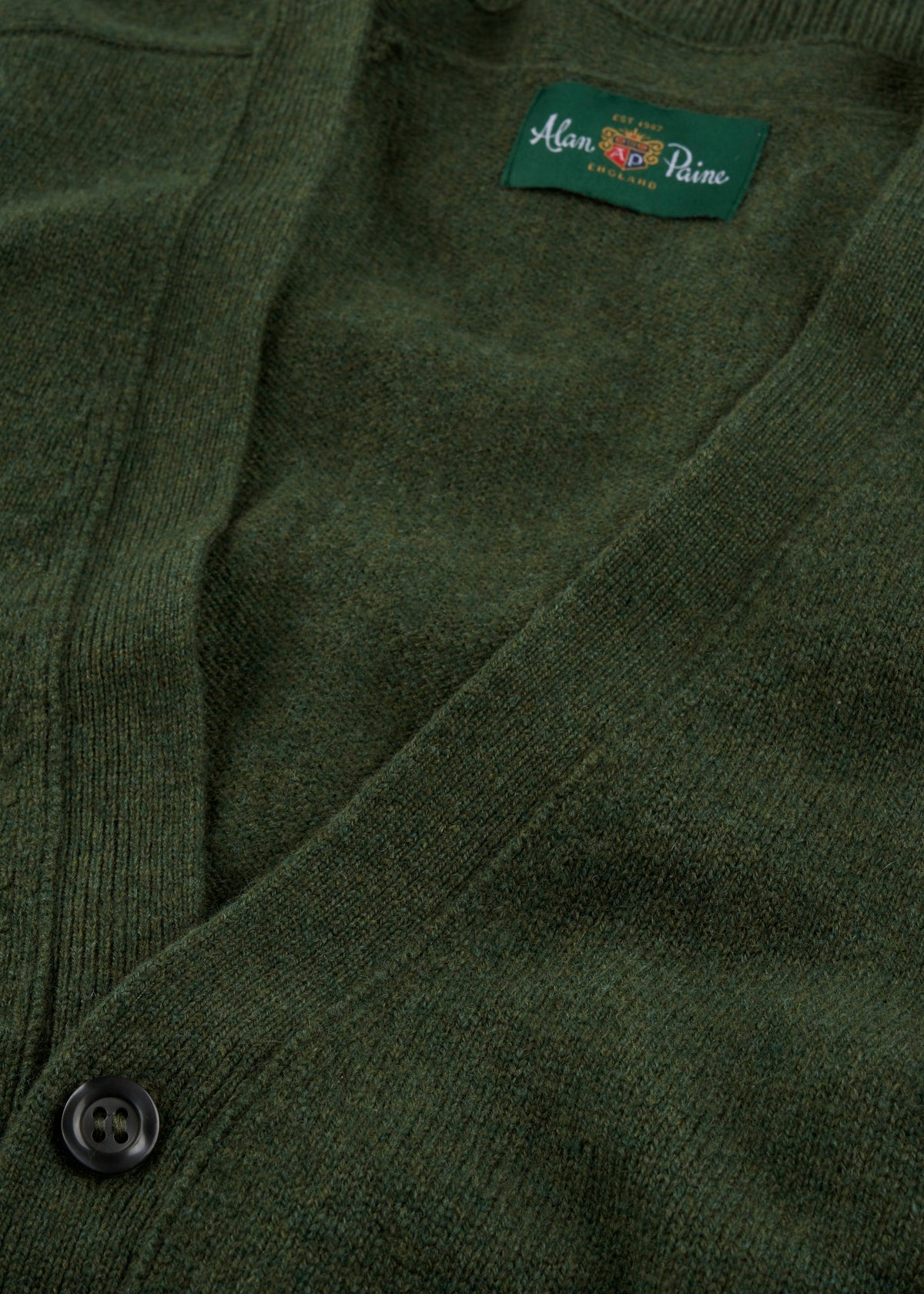 Close-up of the Cornwall Lambswool V-Neck Cardigan in Rosemary with black button and Alan Paine London label inside collar.