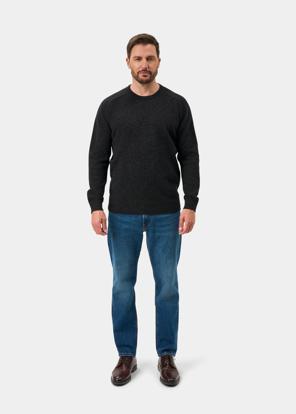 Man facing forward in a Dorset Lambswool Crew Neck Jumper in Charcoal, blue jeans, and brown shoes on plain background.