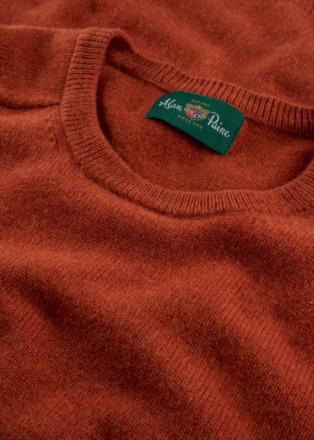 Close-up of Dorset Lambswool Crew Neck Jumper in Ember with green Alan Paine England label and saddle shoulder.