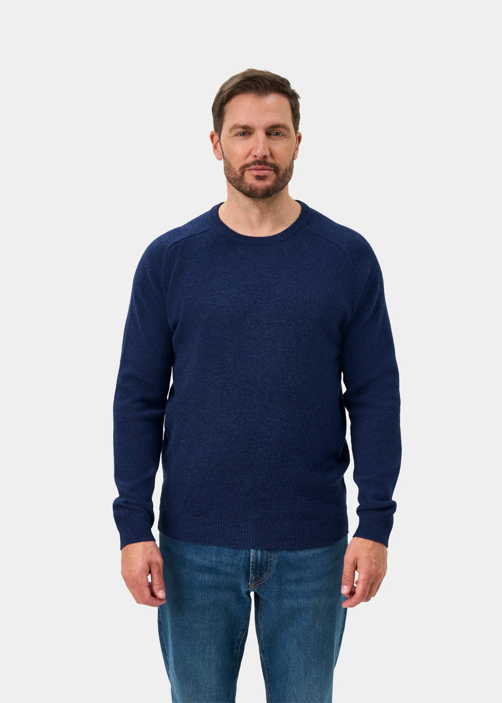 Man wears Lenzie Lambswool Crew Neck Jumper in Rhapsody (Regular Fit) with jeans, facing forward on white backdrop.