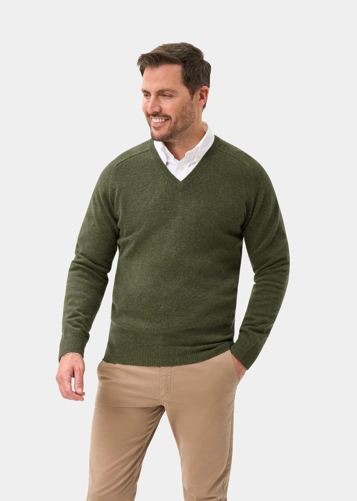 Man in Kilsyth Lambswool V-Neck Jumper in Landscape, over a white shirt and tan pants, smiling against light background.