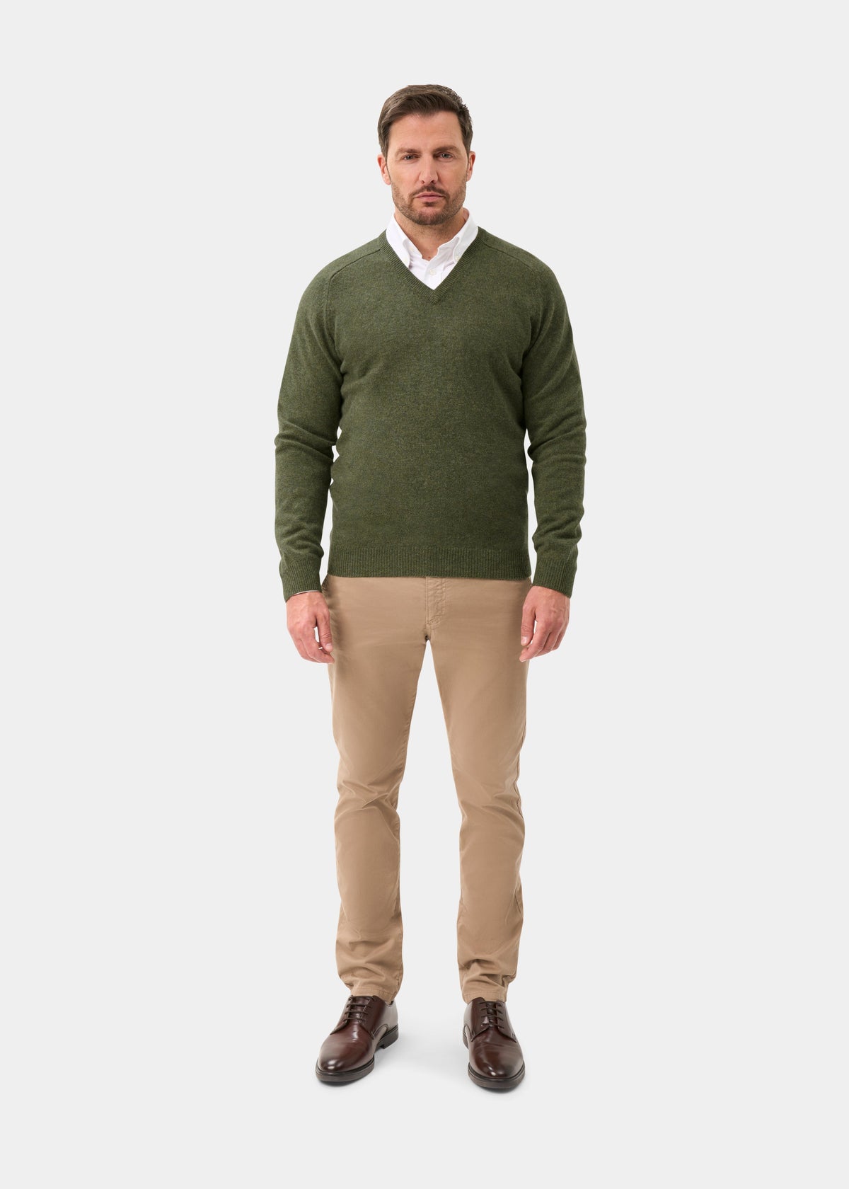 Man wearing Kilsyth Lambswool V-Neck Jumper in Landscape, white shirt, beige pants, brown shoes on white background.