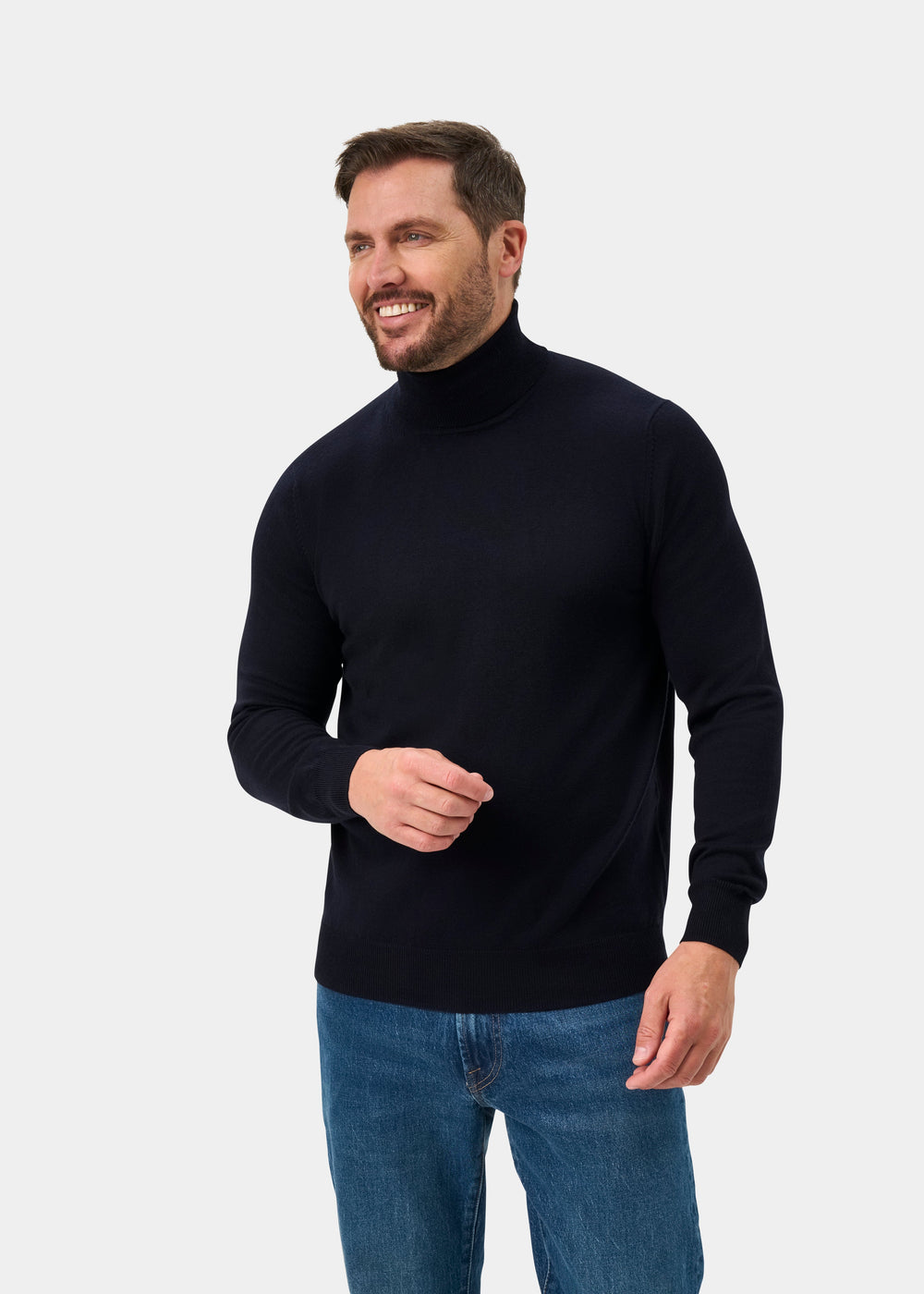 Man in Linton Merino Wool Roll Neck Jumper in dark navy, smiling and looking to the side against plain background.