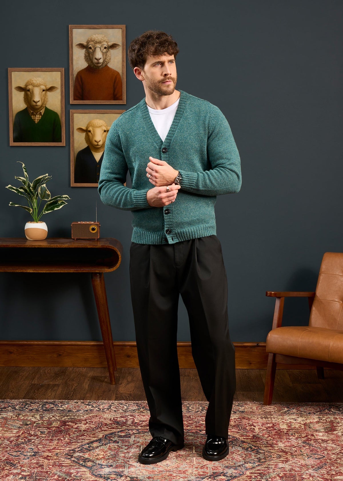 Man in Kinloch Supersoft Shetland Wool V-Neck Cardigan stands in chic room with sheep art and vintage accents.