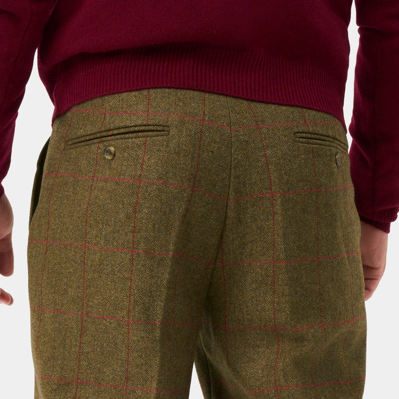 Rear view of a person wearing olive green tweed trousers, burgundy knit socks, and olive green rain boots against a light gray background.
