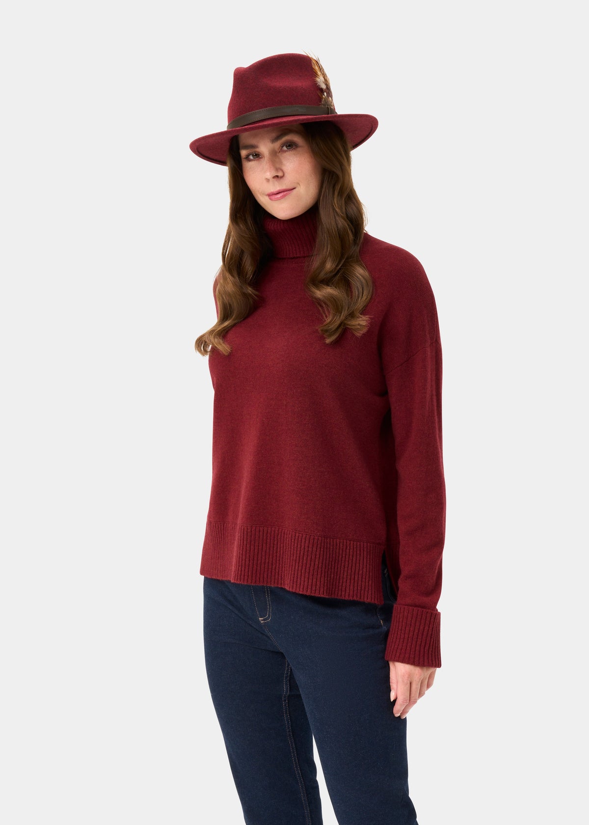 Woman in Alexa Ladies Wool and Cashmere Roll Neck in Berry with matching hat, standing against a plain background.