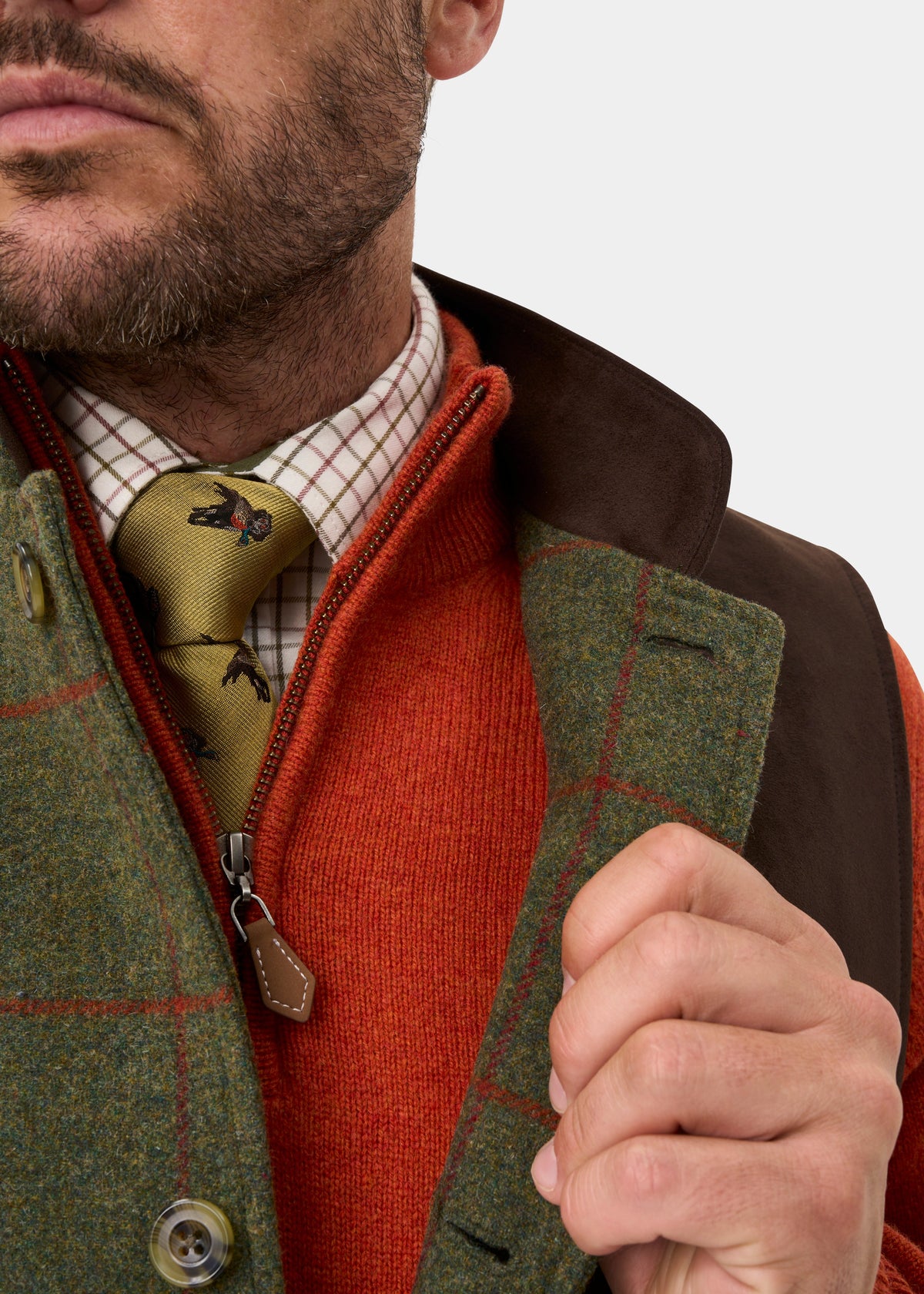 Man in orange sweater, Combrook Tweed Gilet in Reed, check shirt & patterned tie, adjusting his vest.