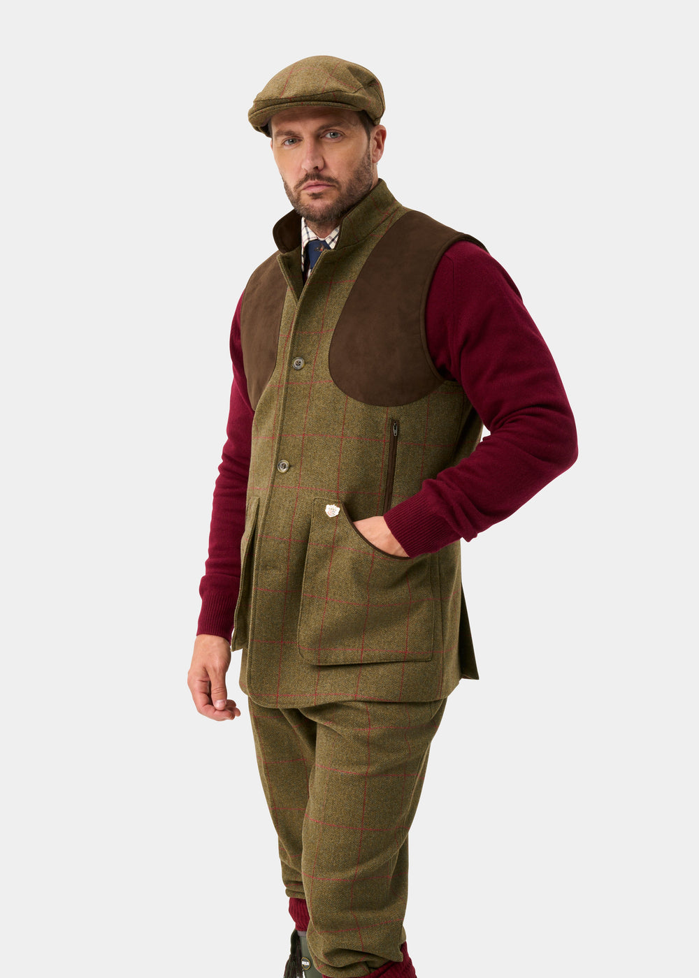 Man in Combrook Men’s Tweed Water Repellent Shooting Gilet in Sage, tweed cap, red shirt, and pants on white background.