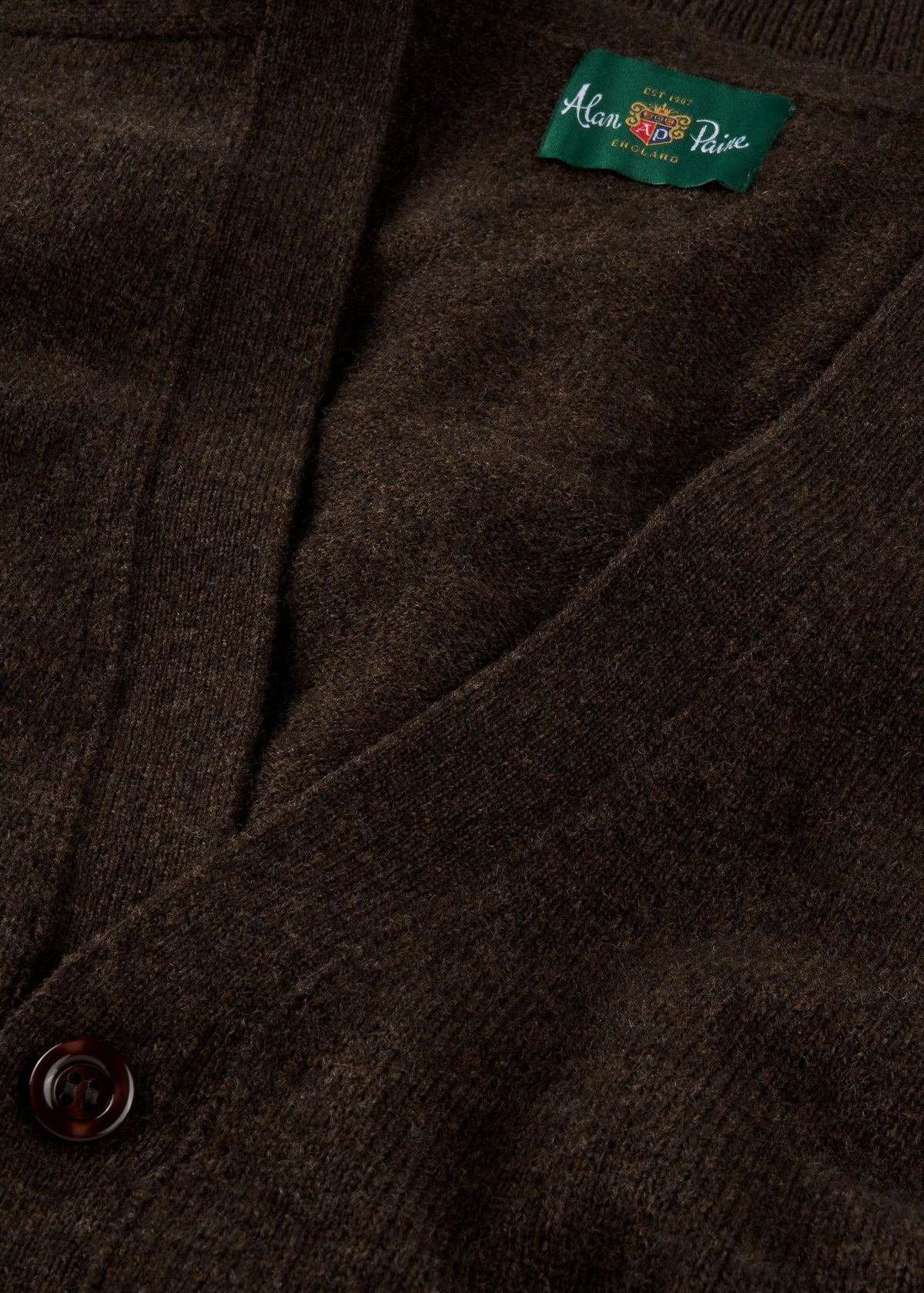 Close-up of Cornwall Lambswool V-Neck Cardigan in Cocoa, classic fit, with a button and green Alan Paine label.