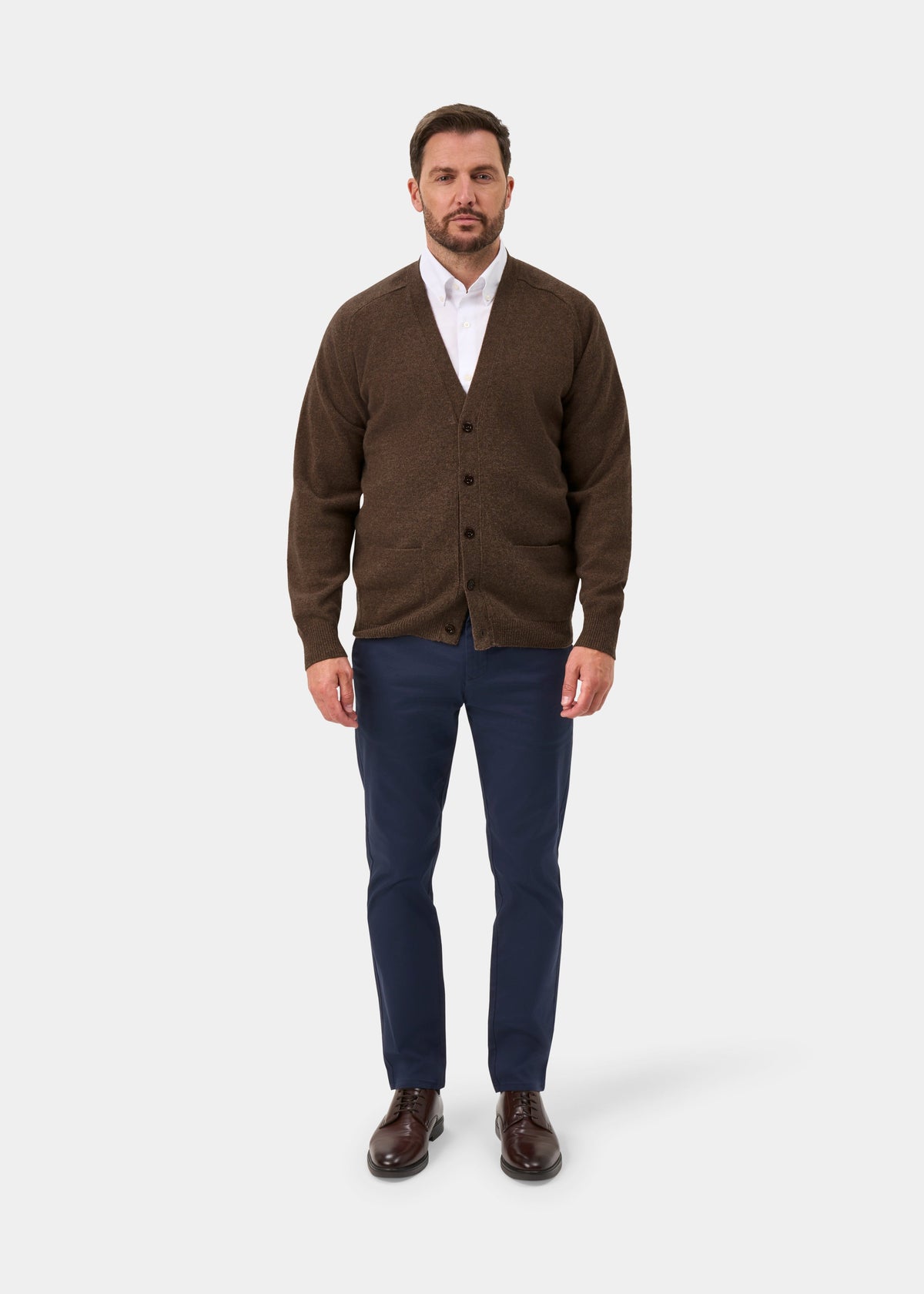 Man in Cornwall Lambswool V-Neck Cardigan in Tobacco, white shirt, blue pants, brown shoes on plain white background.