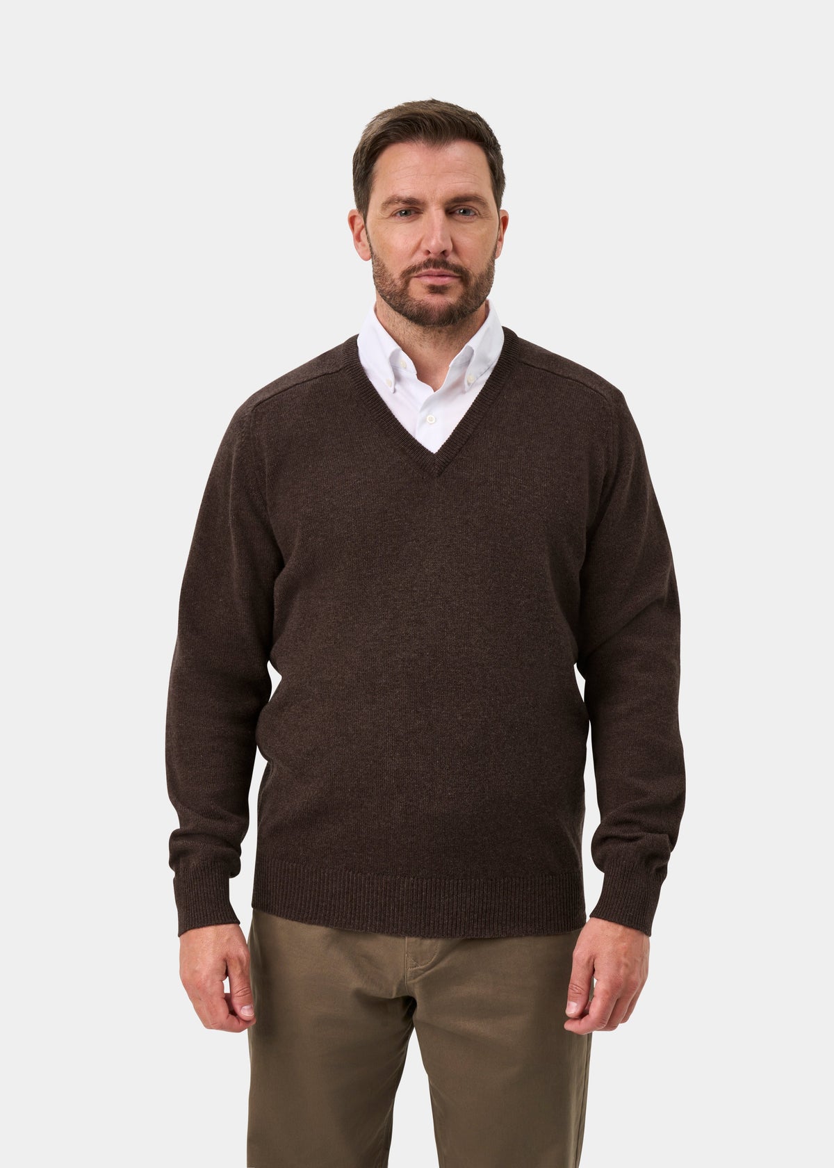 Man in a Hampshire Lambswool V-Neck Jumper in Mocha, white shirt, and brown pants against a plain light background.