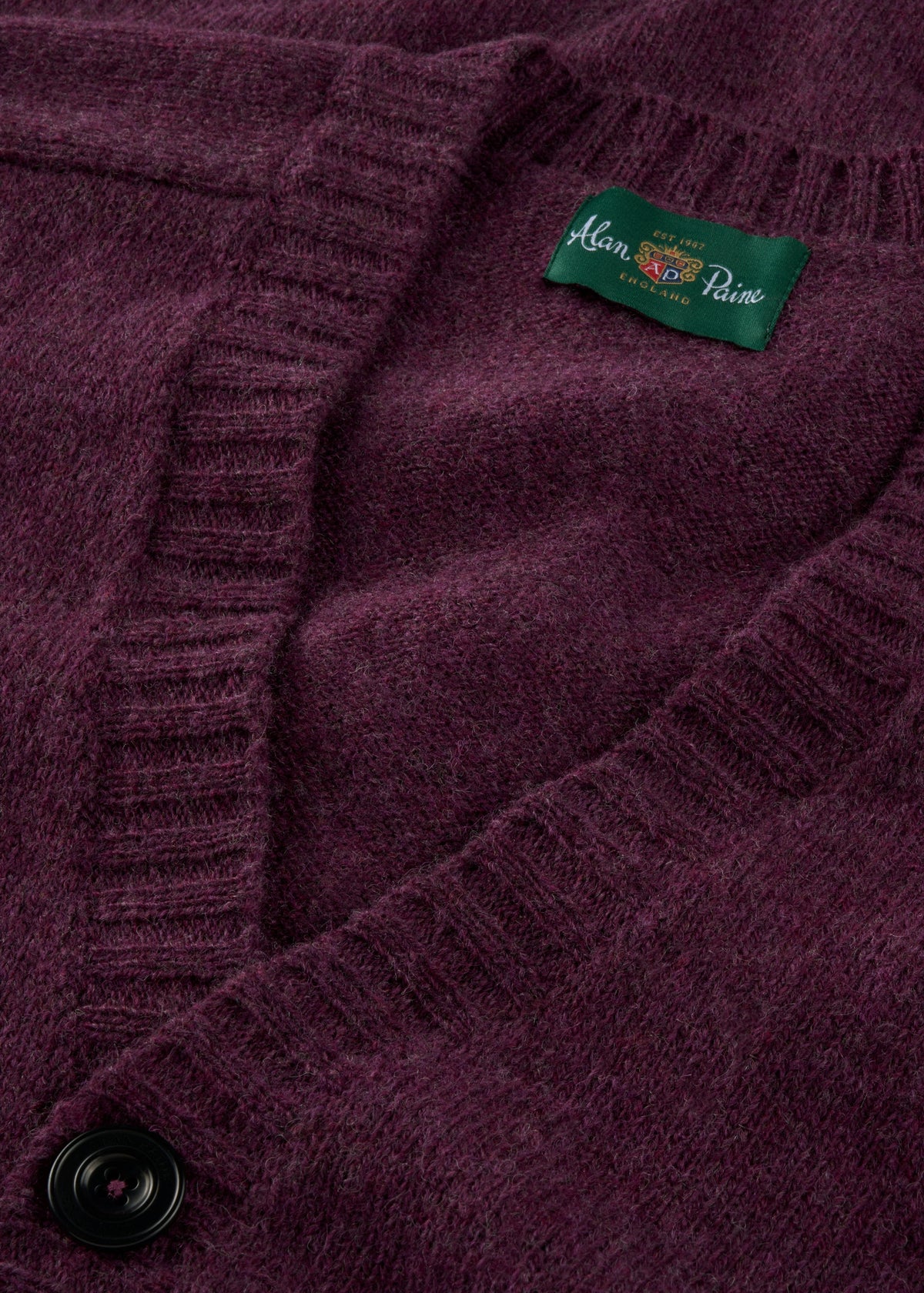 Close-up of the Kinloch Supersoft Shetland Wool V-Neck Cardigan in Elderberry with black button and green label.