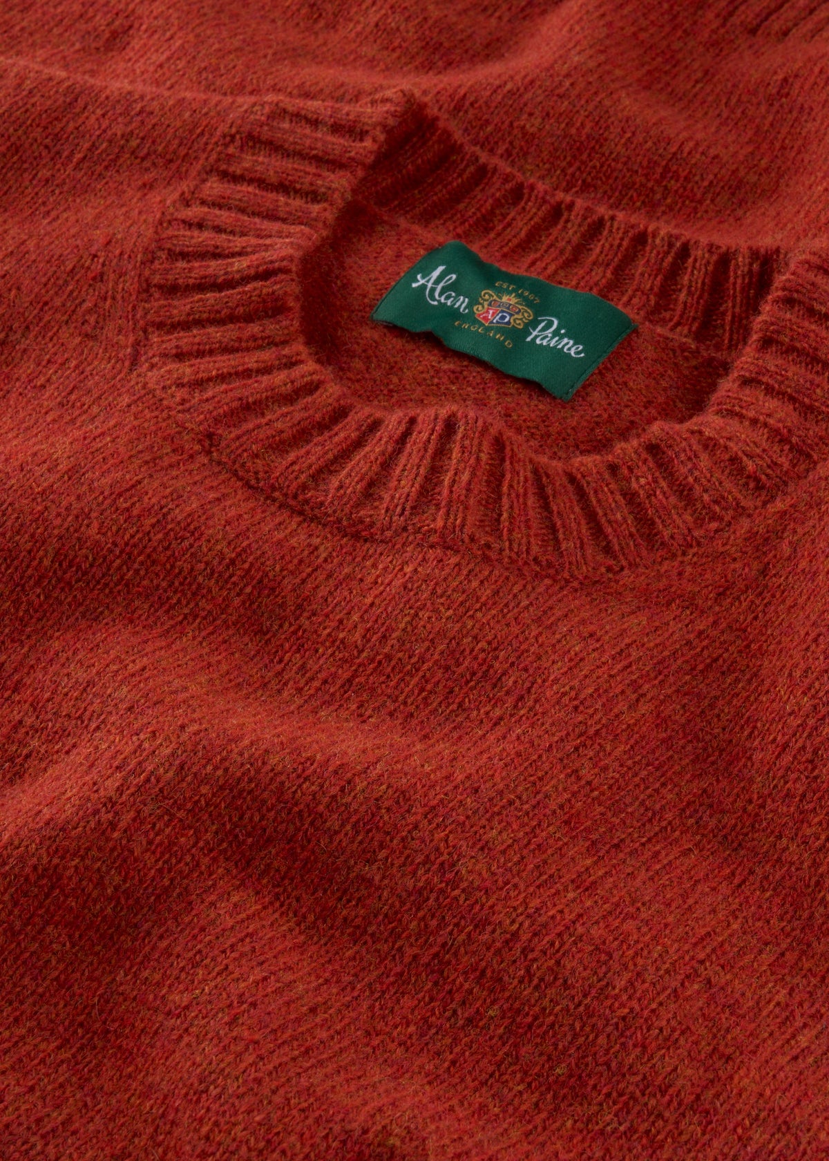 Close-up of a saffron Kinnadie Supersoft Shetland wool jumper with ribbed collar and green Alan Paine label.