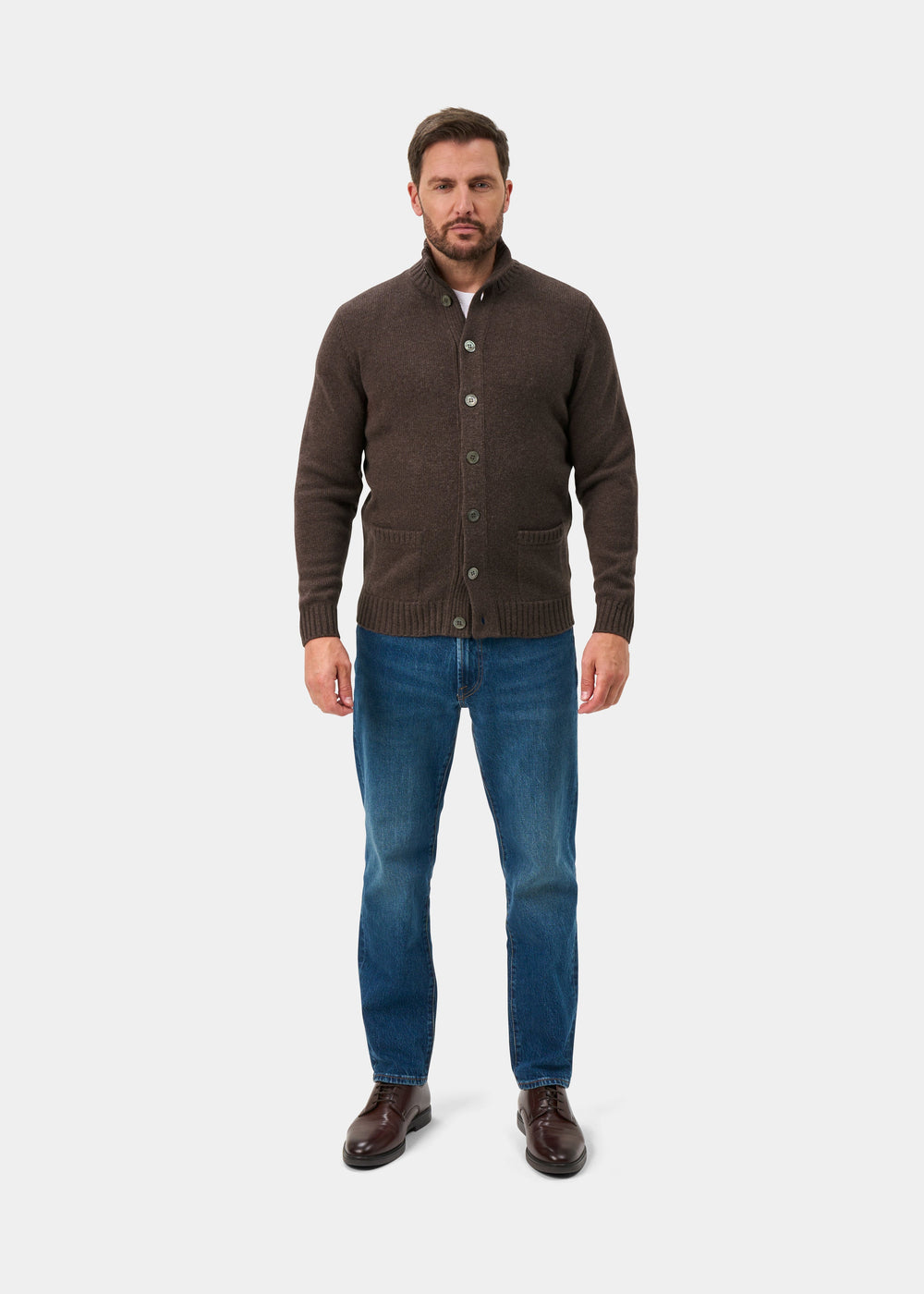 Man wears Landford Lambswool Buttoned Mock Neck Jumper in Mocha, blue jeans, and brown shoes on a white background.