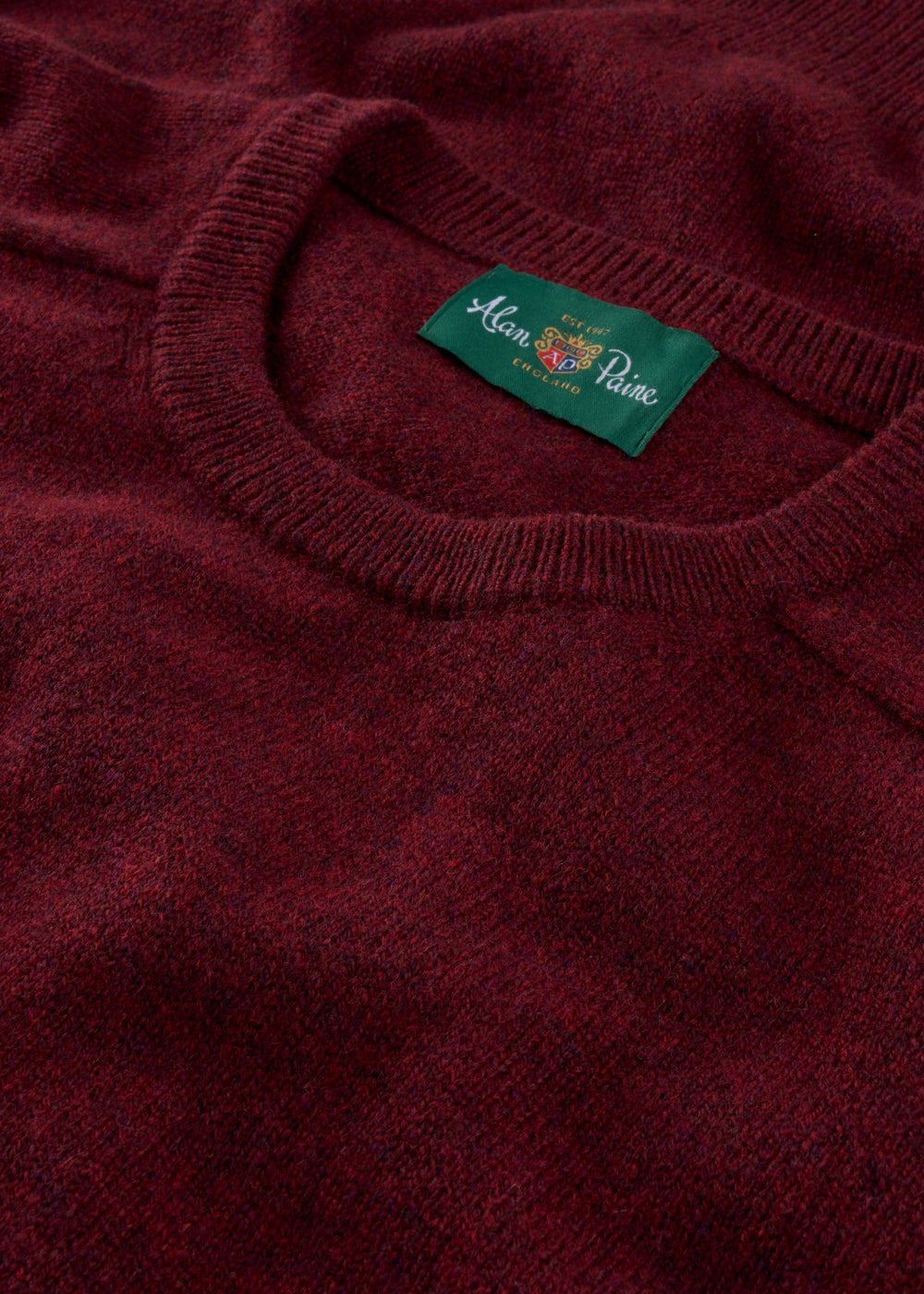 Close-up of the Lenzie Lambswool Crew Neck Jumper in Red Velvet, featuring a green Alan Paine England label.